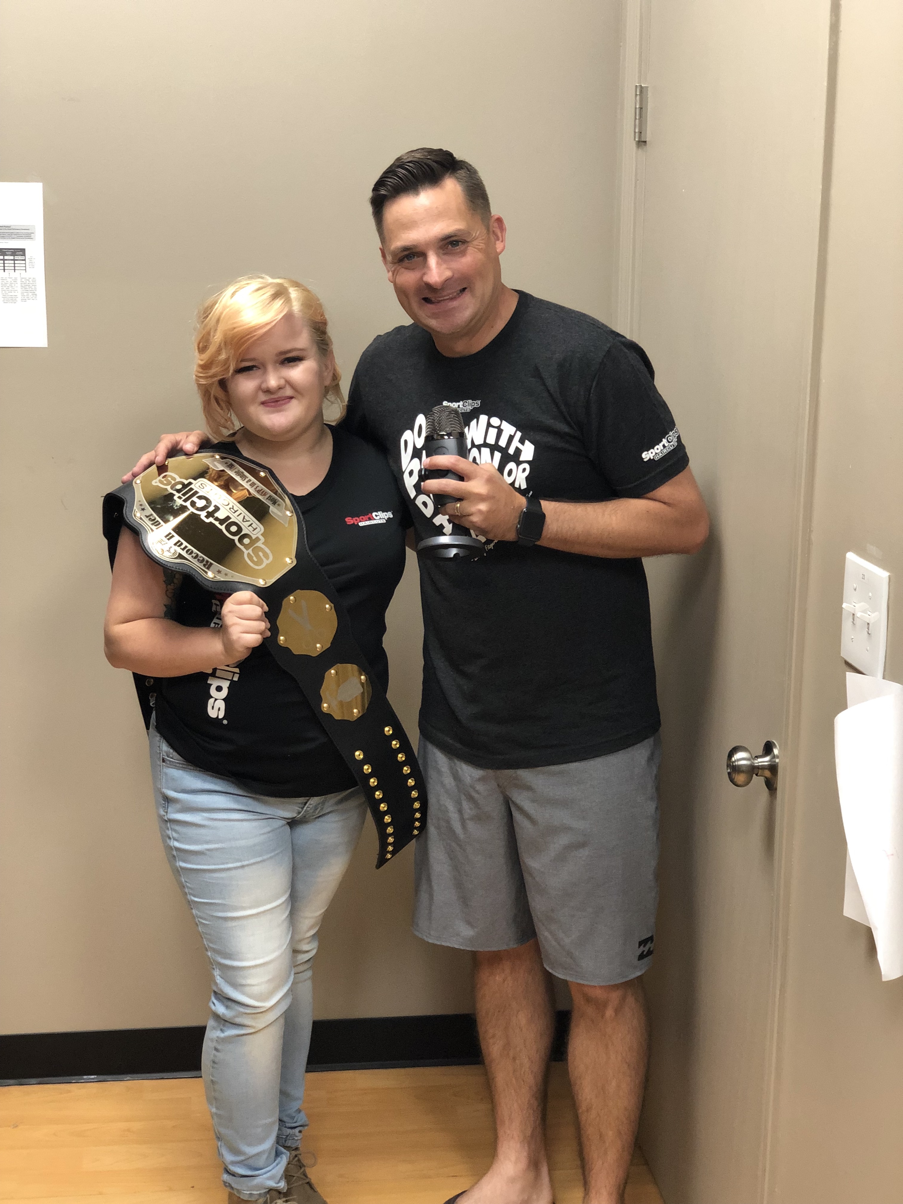 Chad Jordan holding a microphone and Kirsten Buhr holding a championship heavyweight belt